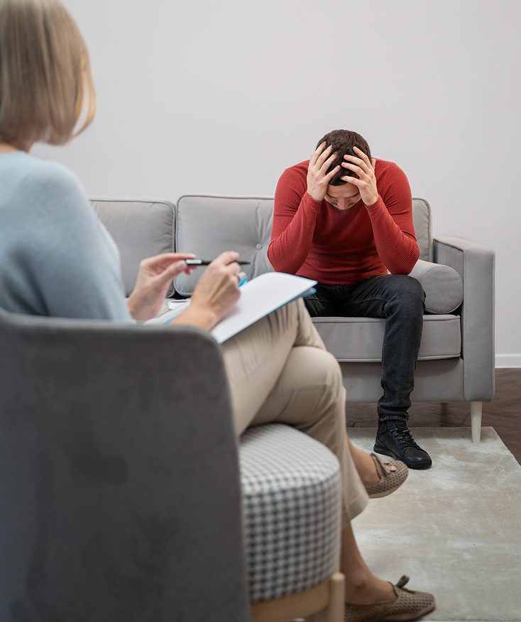 A stressed person sits with their head in hands during a therapy session.